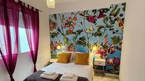 Une chambre à coucher comprenant un lit, des tables de chevet, une lampe suspendue, un banc et une fresque murale à motifs floraux.
