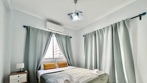 A neatly arranged bedroom with a bed, a bedside table, and an air conditioning unit. - 114 LCA - Stay Mckenzie Mile (Larnaca)