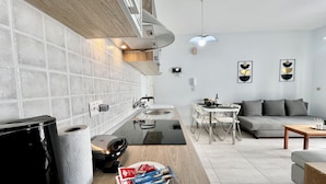 A modern kitchen with a built-in oven, a dining area with a table and chairs, and a living area with a sofa and a coffee table. - 114 LCA - Stay Mckenzie Mile (Larnaca)