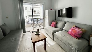 A modern living room with a grey sofa, a wooden coffee table, and a balcony with a table and chairs. - 114 LCA - Stay Mckenzie Mile (Larnaca)