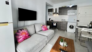A modern living room with a grey sofa, a flat-screen TV, and a wooden coffee table with a remote control. - 114 LCA - Stay Mckenzie Mile (Larnaca)