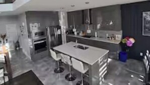 Una cocina moderna con una isla central, taburetes de bar y vistas al salón.
