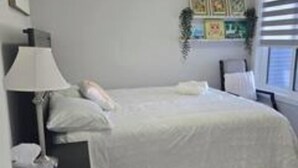 Un dormitorio con cama, mesita de noche, lámpara y ventana con persianas.