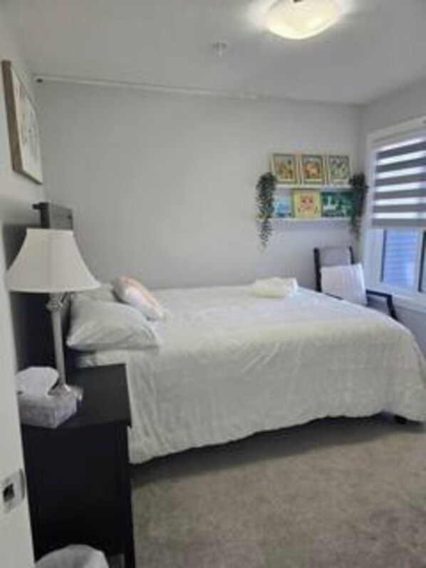 A bedroom with a bed, bedside table, lamp, and a window with blinds. - Spacious Edmonton Family Rental (Edmonton)