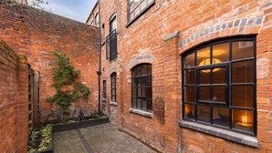 A brick building with a courtyard, featuring a large arched window and a small garden area. - Enamel Works - The Bellows (West Midlands)
