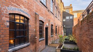 A narrow alleyway with brick buildings, arched windows, and a small garden area. - Enamel Works - The Bellows (West Midlands)