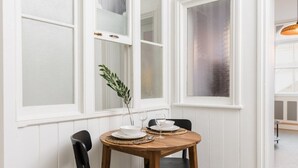 A dining area with a round wooden table set for two, white walls, and large windows with frosted glass panes. - Enamel Works - The Stronghold (West Midlands)
