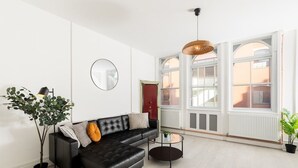 A modern living room with a black leather sofa, a round mirror, and a hanging wicker light fixture. - Enamel Works - The Stronghold (West Midlands)