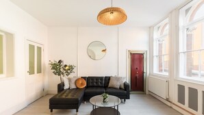 A modern living room with a sectional sofa, a round coffee table, and a large window with a view. - Enamel Works - The Stronghold (West Midlands)