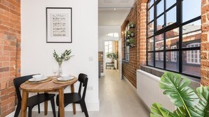Un coin repas avec un mur en briques, une œuvre d’art encadrée et une fenêtre agrémentée de plantes.