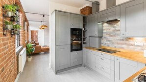 Une cuisine moderne avec des armoires grises, un mur de fond en briques et un plan de travail en bois.