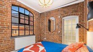 Une chambre avec un mur en briques, une grande fenêtre, un lit avec une literie à motifs et un miroir.