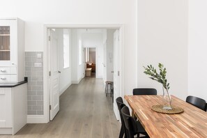 A modern kitchen with white cabinetry, a wooden dining table with chairs, and a vase with greenery. - Spacious Grade II penthouse | Private entrance (West Midlands)