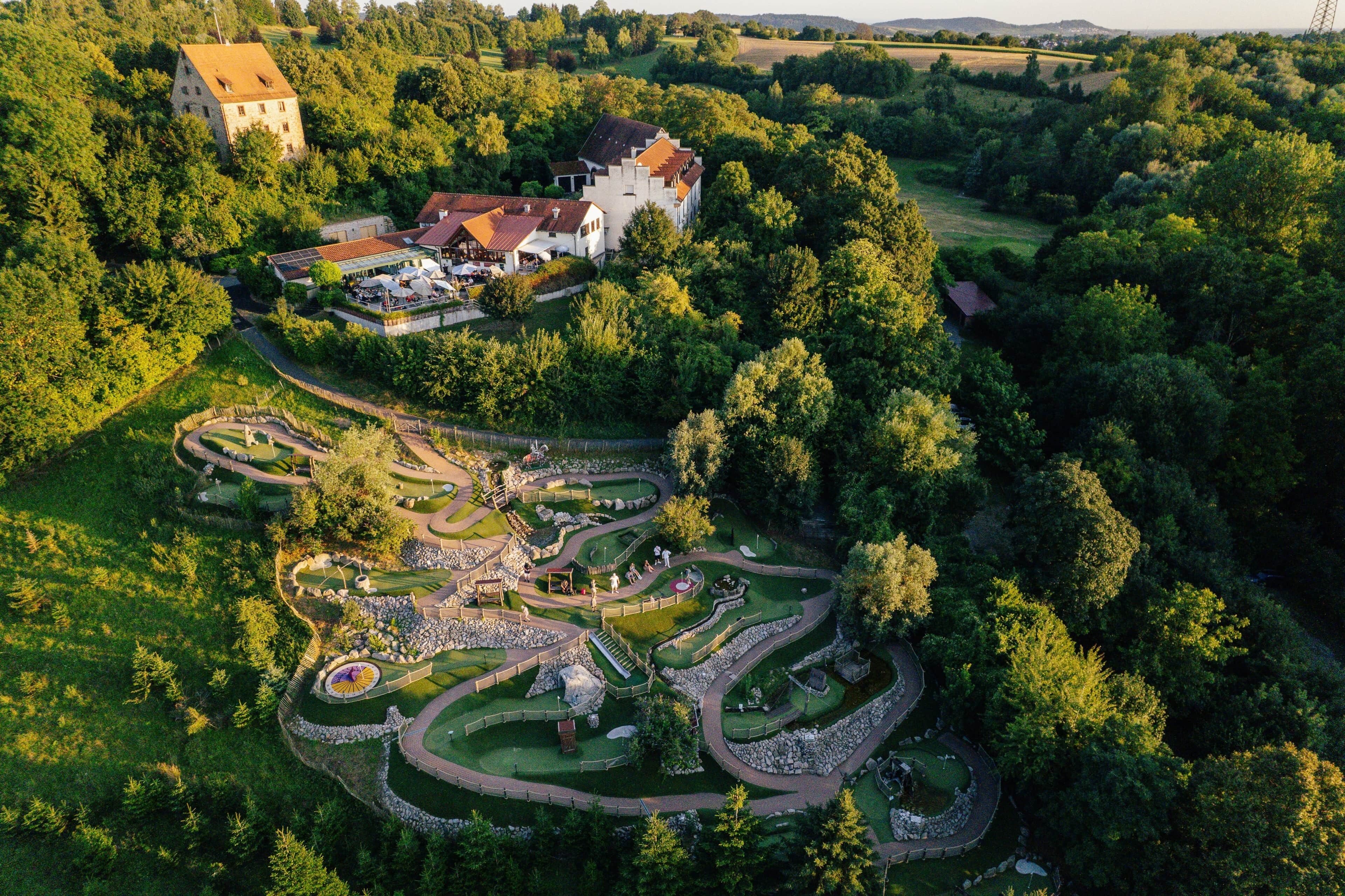 An aerial view of a large estate with a winding garden path, a central fountain, and a large building with a red roof.
