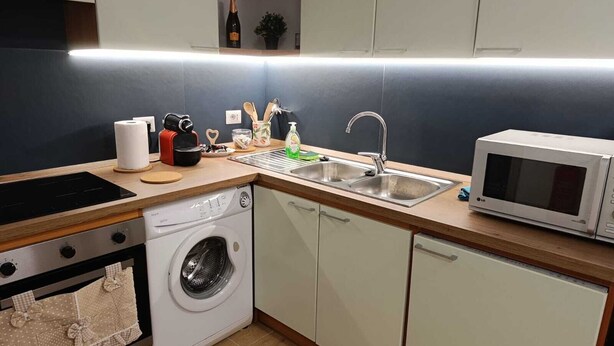 Ett kompakt kök med tvättmaskin, mikrovågsugn, diskho och diverse köksredskap.