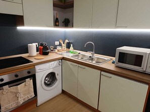 A compact kitchen with a washing machine, microwave, sink, and various kitchen utensils. - Ricc House, Rome (Roma)