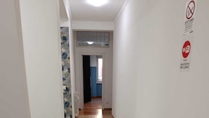 En hall med trägolv, vita väggar och en dörr som leder till ett annat rum. Det finns skyltar som visar var man kan använda Wi-Fi och att det är rökfritt i området.