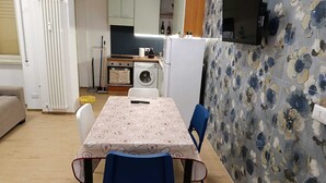 Ett kompakt kök med tvättmaskin, ett matbord med stolar och en TV som är monterad på väggen.