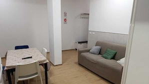 Ett litet, väl upplyst rum med ett matbord och stolar, en soffa med kuddar och en whiteboard med en skylt som förbjuder rökning.