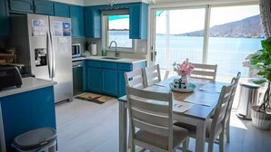Moderni keittiö, jossa on siniset kaapit, valkoiset tuolit ruokailutilassa ja näkymä järvelle.