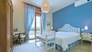 Quarto com cama, uma cadeira, mesa de cabeceira e janela com cortinas.