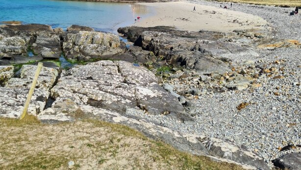 Una playa rocosa con aguas azul turquesa y una orilla de arena.
