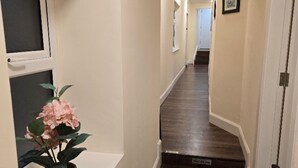 Un pasillo con suelo de madera, una planta en maceta y una puerta con un letrero.