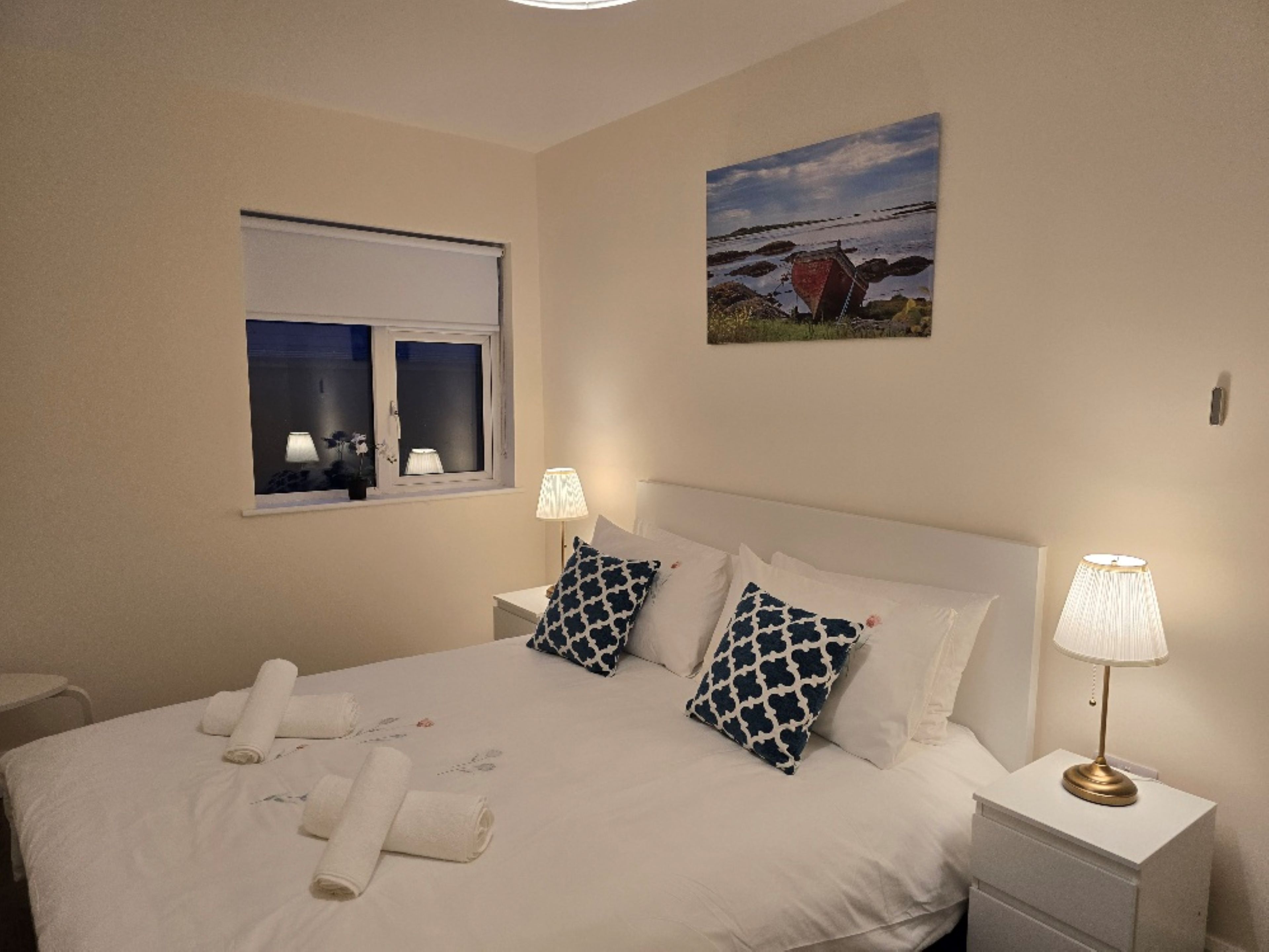 A neatly made bed with pillows, a bedside lamp, and a window with a view of the outside.