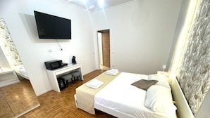 A hotel room with a bed, a desk with a flat-screen TV, a microwave, and a coffee maker. - Gregory Lem collection (Rome)