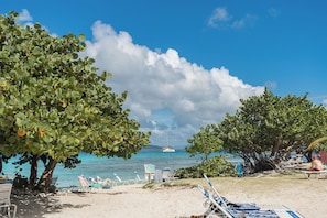 Ein Strand mit Liegestühlen, einem Boot im Wasser und blauem Himmel.