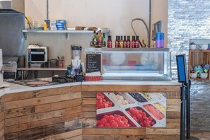 Mostrador de comida con diferentes salsas y condimentos, un menú en una pizarra y un terminal de pago digital.