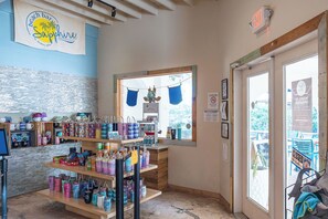 Un bar con temática de playa, con un letrero que dice "beach bar Sapphire", estantes llenos de bebidas coloridas y una ventana con cortinas azules.