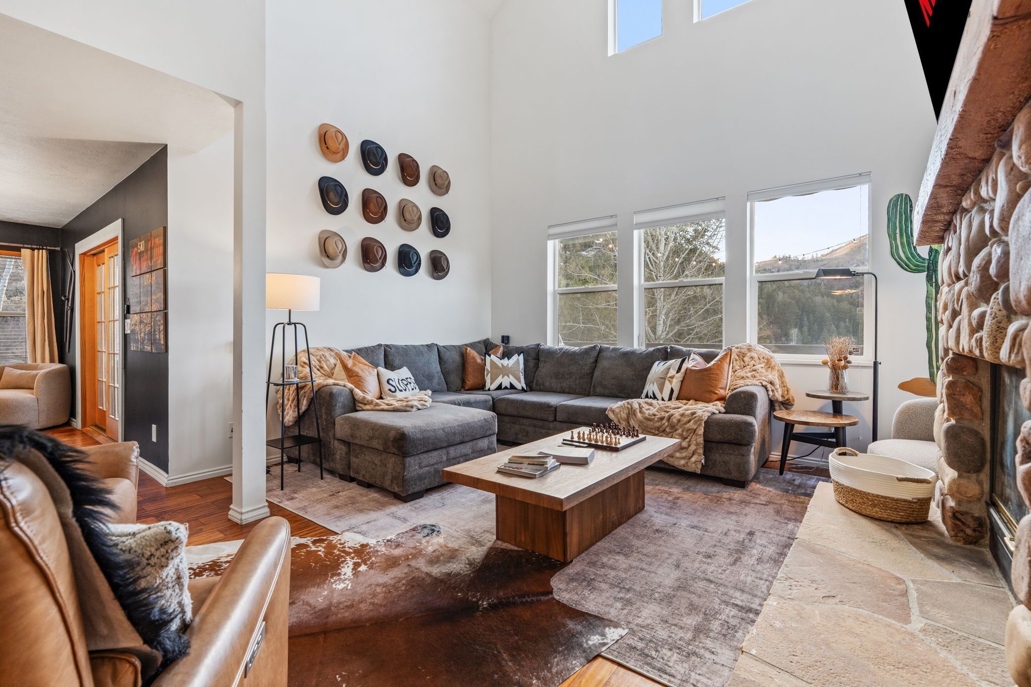 A spacious living room with a large gray sectional sofa, a wooden coffee table, and a wall adorned with various hats.