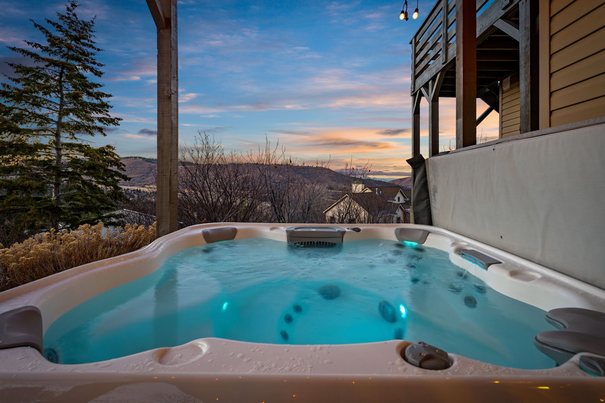 A hot tub with a view of a house and hills in the background.