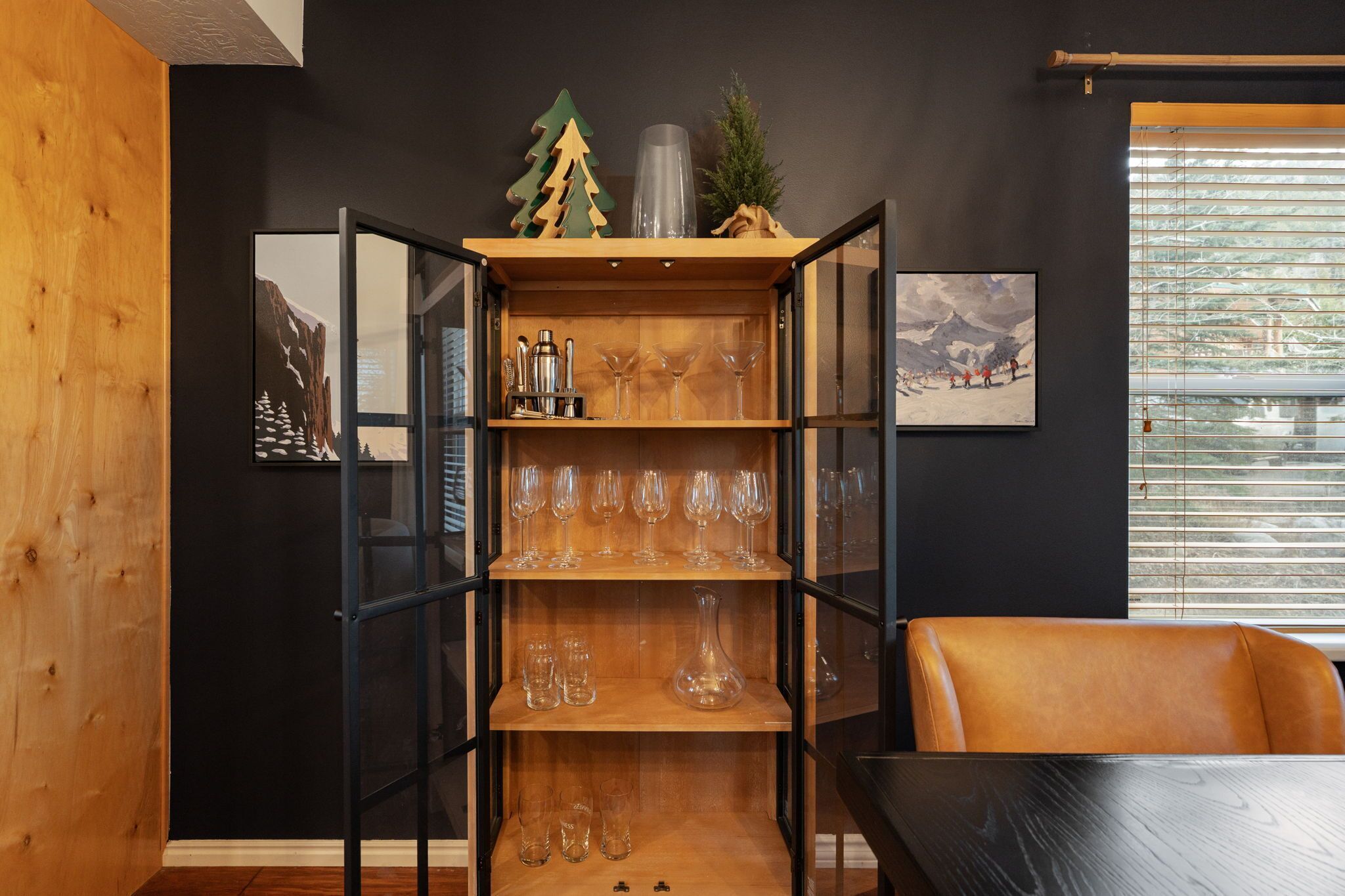 Ein Essbereich mit Holztisch und Stühlen, einem Glastischschrank mit Weingläsern und Flaschen sowie gerahmten Kunstwerken an den Wänden.