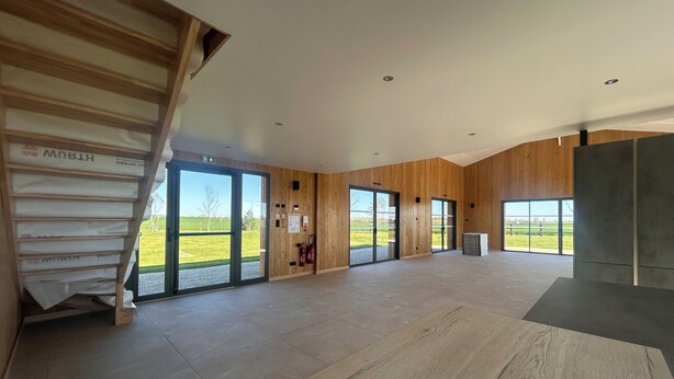 A spacious interior with a wooden staircase, large sliding glass doors, and a view of the outdoors.