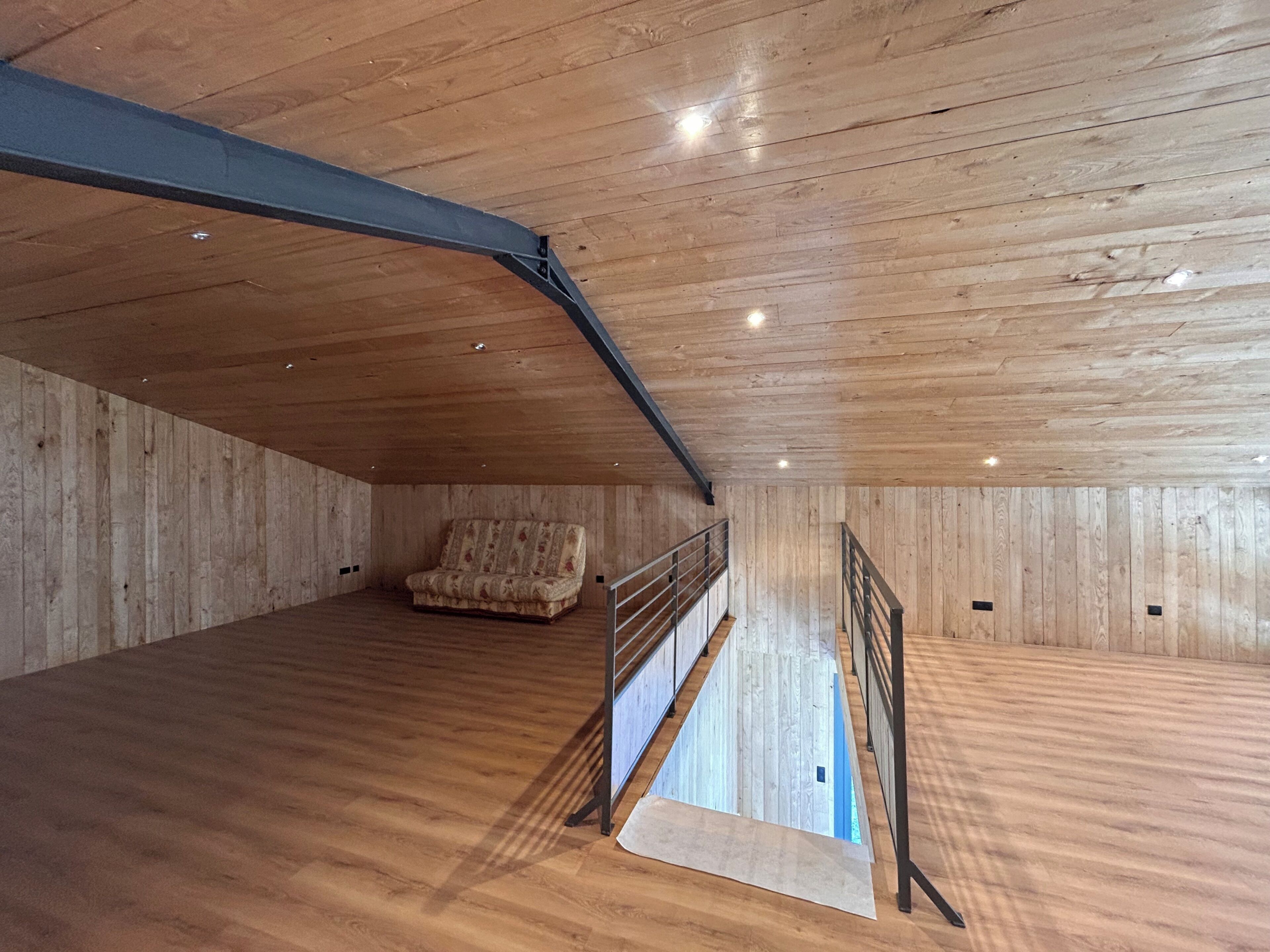 Une pièce mansardée spacieuse, avec des murs en bois et un plafond en pente, comprenant un canapé et un escalier.