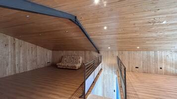 Une pièce mansardée spacieuse, avec des murs en bois et un plafond en pente, comprenant un canapé et un escalier.