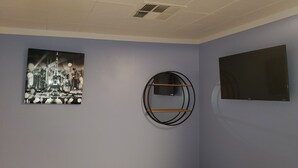 A room with a cityscape painting, a circular shelf with a TV, and a flat-screen TV on the wall. - Compact Studio Lovely, Privacy Affordable safe And Quite #3 (Phoenix)