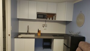 A compact kitchen with white cabinets, a microwave, and a sink. There is a small countertop and a chair in the foreground. - Compact Studio Lovely, Privacy Affordable safe And Quite #3 (Phoenix)