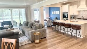 Una sala de estar moderna con un sofá grande de color gris, una mesa de centro de madera y un comedor con taburetes de bar.