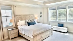 Un dormitorio con una cama grande, mesitas de noche, un banco y una ventana con persianas.