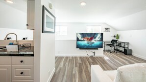 Ein modernes Wohnzimmer mit Flachbildfernseher, einem Essbereich mit Küchenzeile und einem Arbeitsplatz mit Schreibtisch und Stuhl.