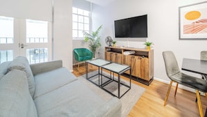 A modern living room with a grey sofa, a wooden TV stand, and a dining table with chairs. - Host Stay Apartment 3 Stanley Street (Liverpool)