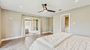 Un dormitorio con una cama grande, un ventilador de techo y vista al exterior por un ventanal corredizo.