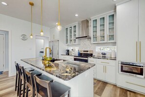 A modern kitchen with white cabinets, a marble island, and gold fixtures. - Modern Living in Texas! Home 2 Blocks to Lake LBJ (Granite Shoals)