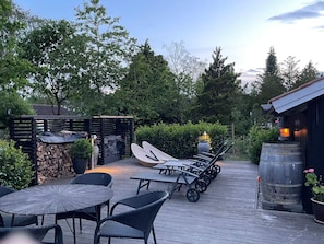 A wooden deck with outdoor furniture, a stone wall, and a wooden barrel. - 5 Star Holiday Home in Gilleleje (Gilleleje)