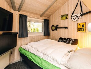 Et soveværelse med en seng, et vindue, et fjernsyn og guitarer på væggen.