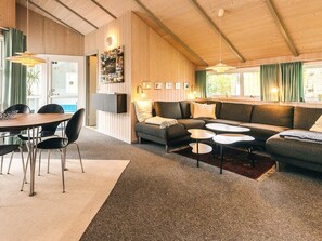 Un soggiorno accogliente con soffitto in legno, una zona divani, un tavolo da pranzo con sedie e una TV a muro.