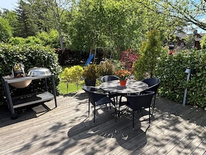 En træterrasse med et rundt bord og stole, en grill og en rutchebane i baggrunden.